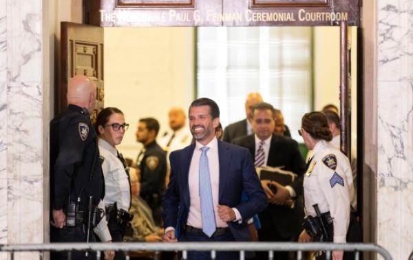 Do<em></em>nald Trump Jr (center) smiles as he exits the courtroom during a break in his testimony in the o<em></em>ngoing civil fraud trial being litigated in New York