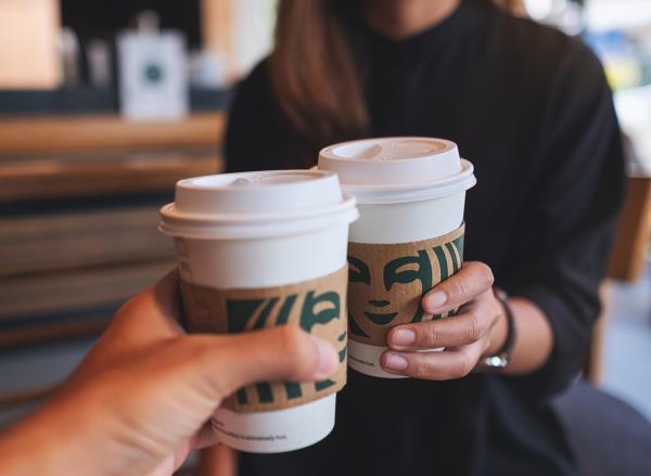 Closeup of a couple people holding and cl<em></em>inking two cup of hot coffee at Starbucks coffee shop